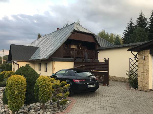 Zdjęcie przedstawia wejście do mieszkania, odgrodzoną strefę dla gości oraz miejsce parkingowe