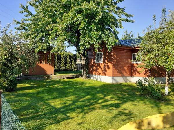 Domek stoi na terenie zadrzewionym w drzewa owocowe.